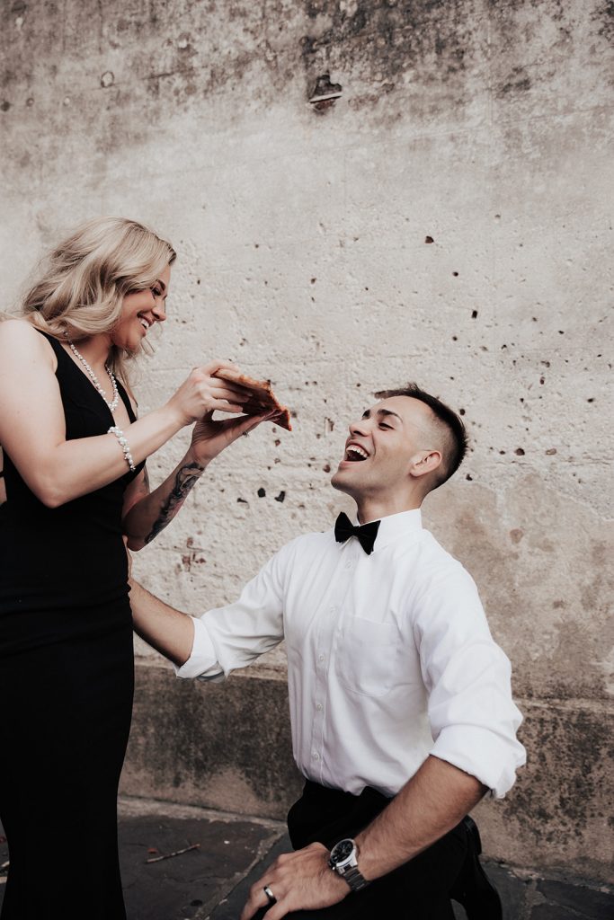 Woman in black dress feeding man with pizza at their engagement session