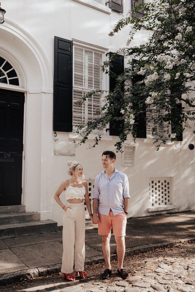 couple standing on famous cobblestone streets in Charleston with white house in background