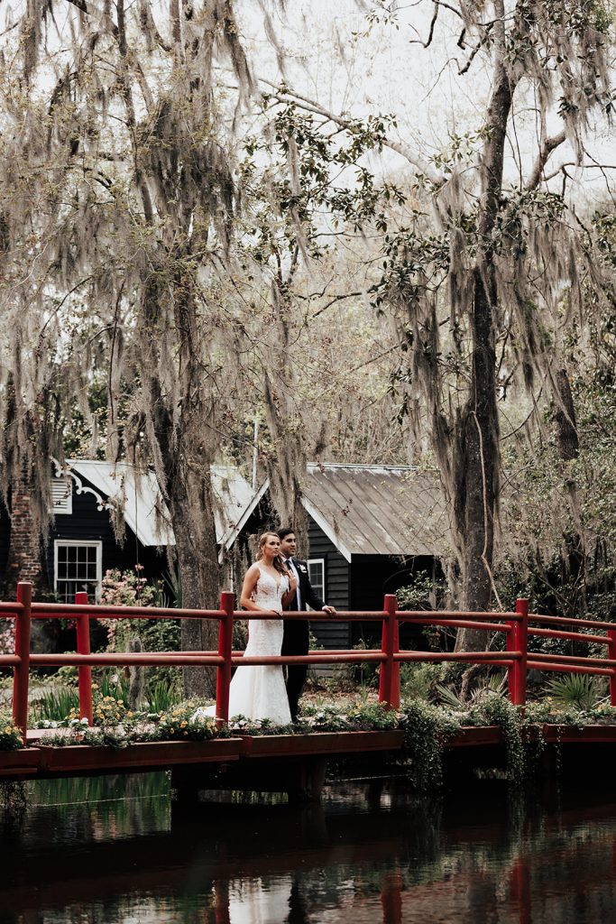 Bride and groom standing on red bride at Magnolia Plantation looking at pond
