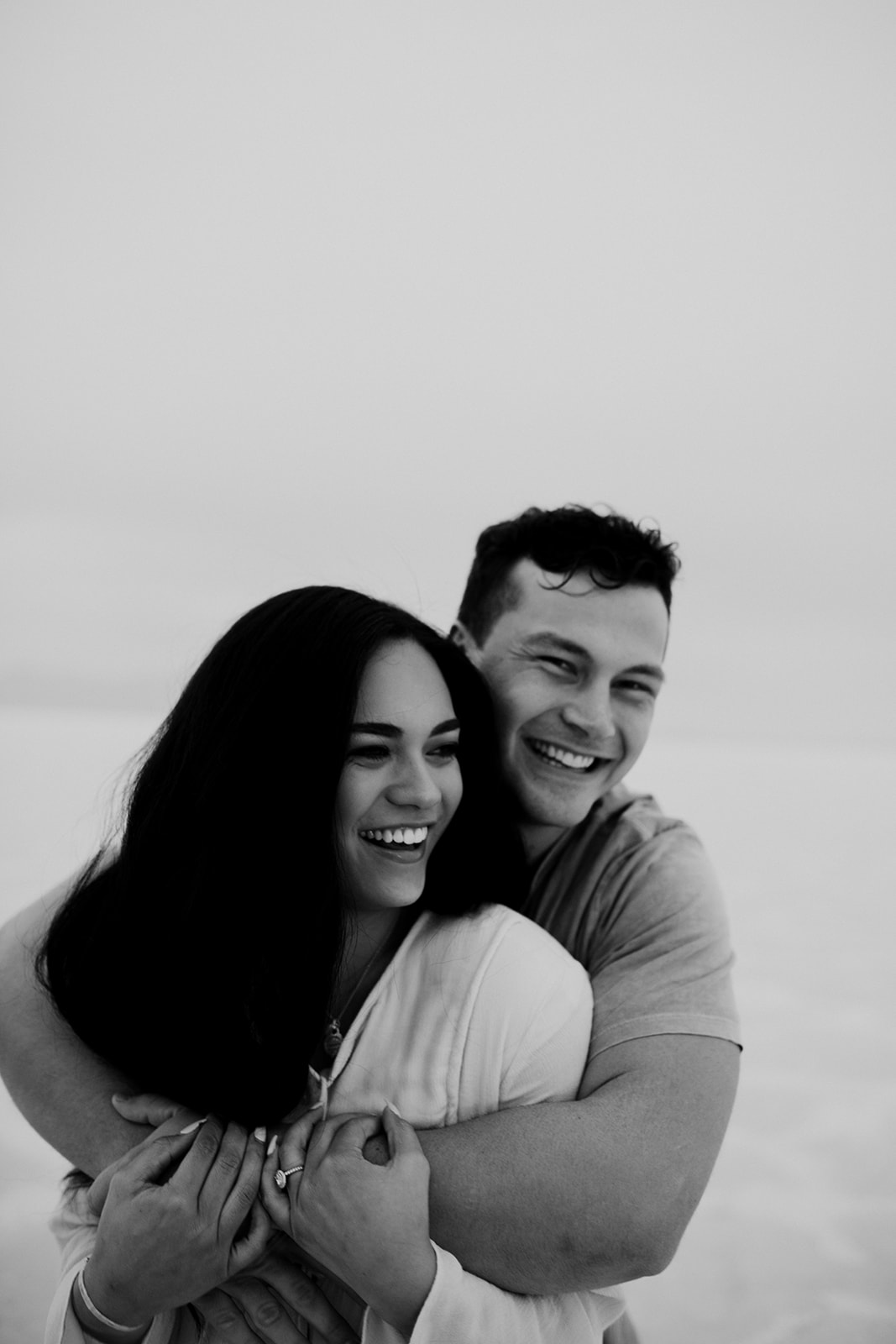 Back and white photo of couple. Man wrapping arms around woman while both smiling at Bonneville Salt Flats engagement