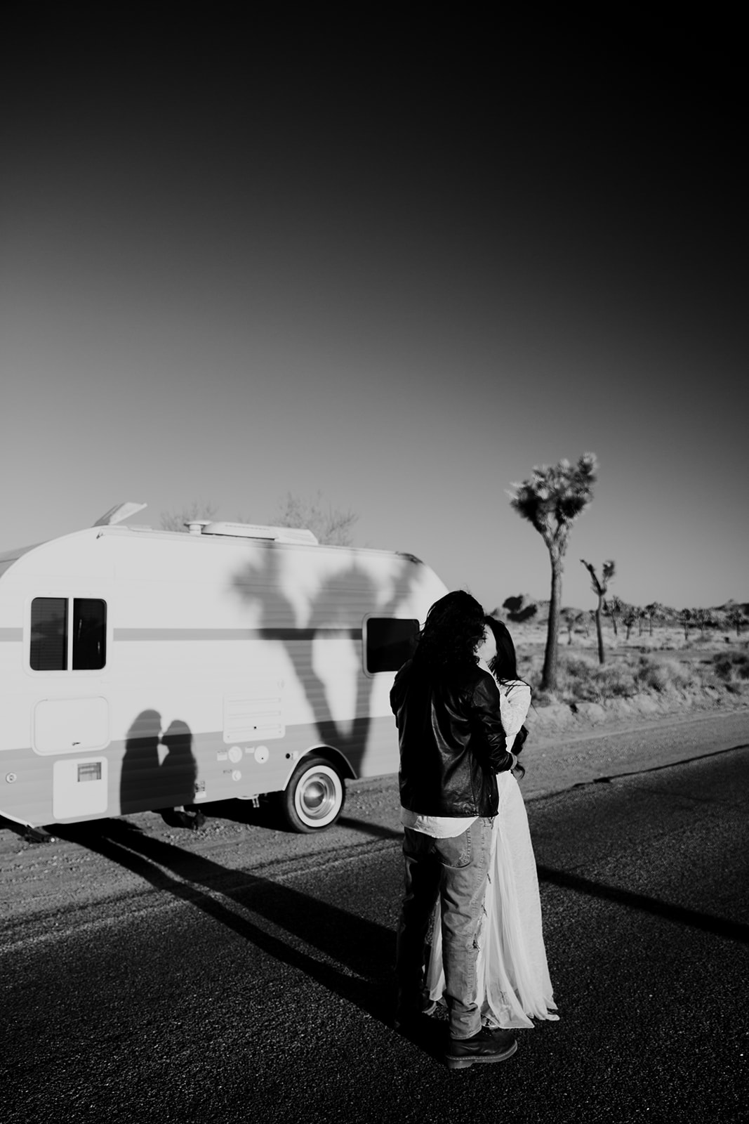 Couple kissing in front of camping trailer casting shadow