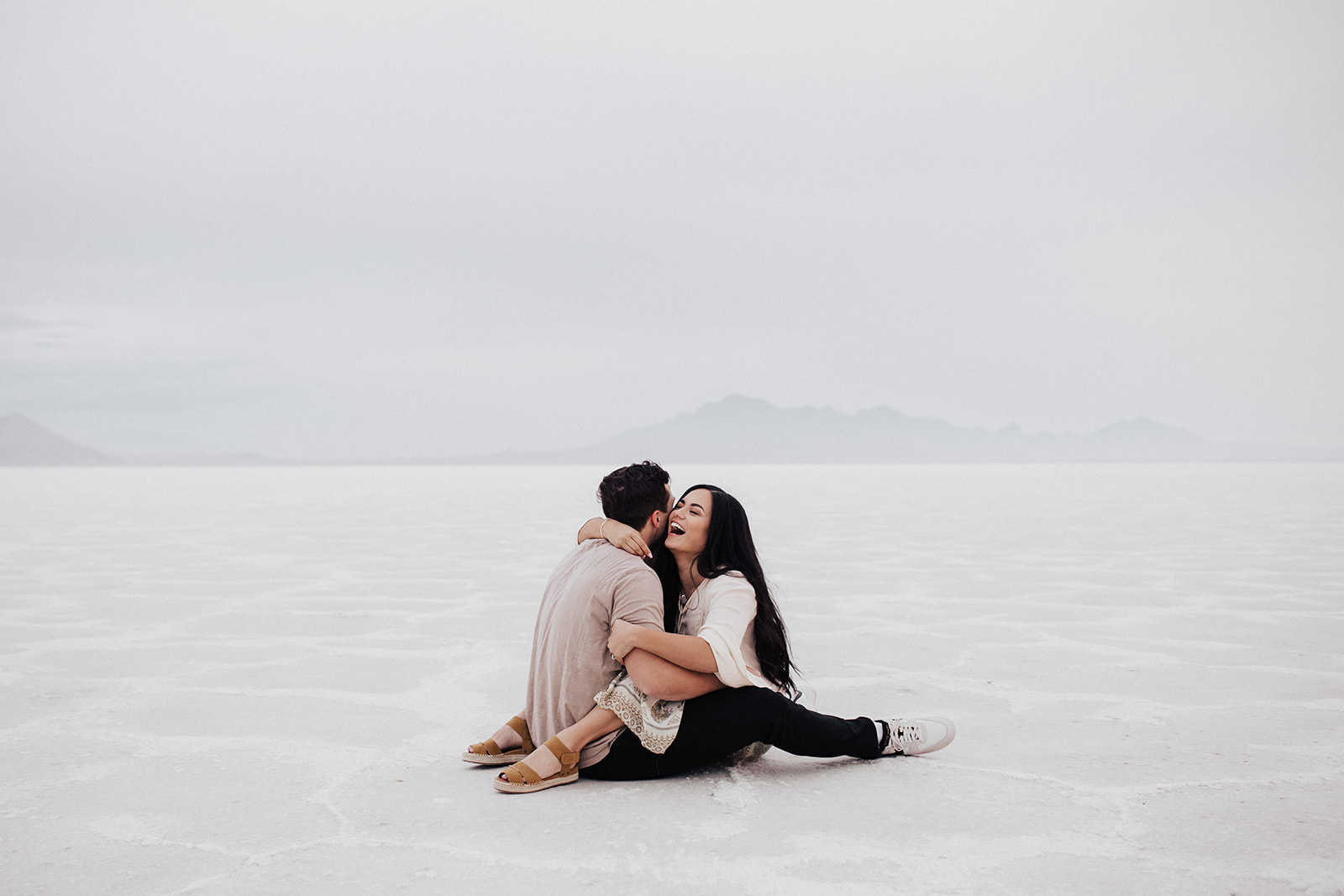 couple sitting on white salt flats during Engagement Photos at Bonneville Salt Flats session