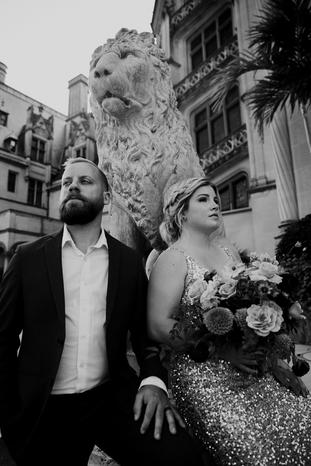 Couple standing side by side with hugh lion head in the background.