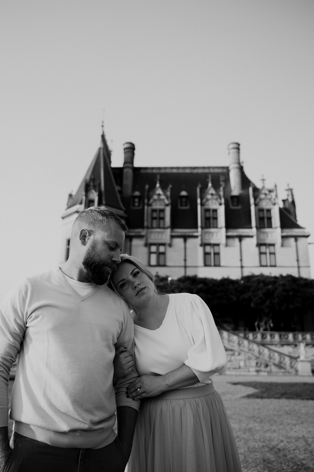 Black and white photo of couple. Woman leaning head on mans shoulder. Biltmore estate in the background. Photo taken during Biltmore Estate photo session