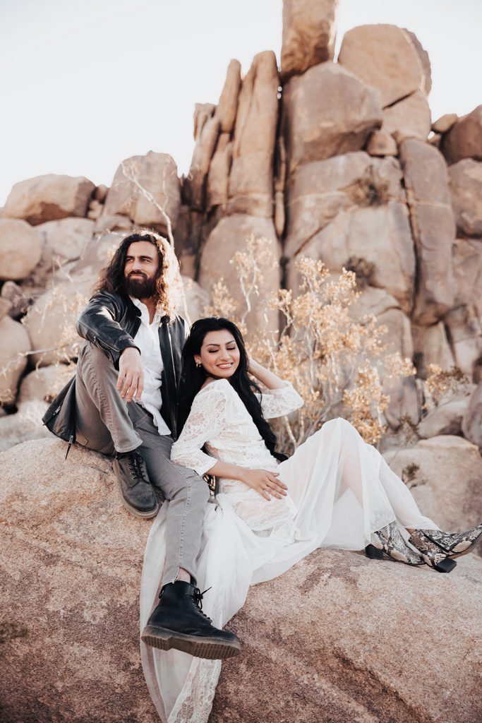couple sitting on rock in edgy outfits for Joshua Tree Engagement