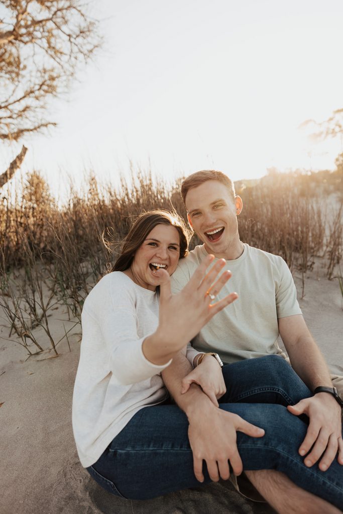 couple smiling at camera and woman shows engagement ring at folly beach proposal