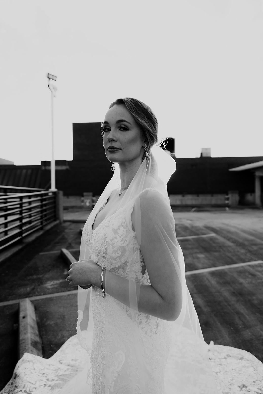 Bride standing on top of parking garage looking into camera. Edgy bridal photo vibe.