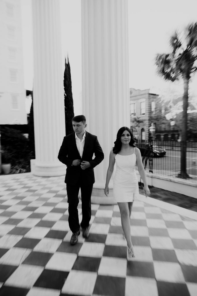 Chic couple walking on chess board style floor with white column in background in Charleston 