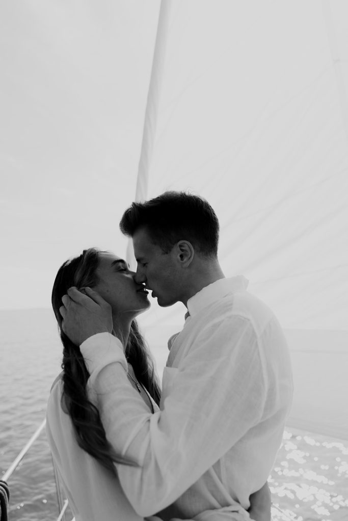 Couple sharing a kiss in front of white sail of boat