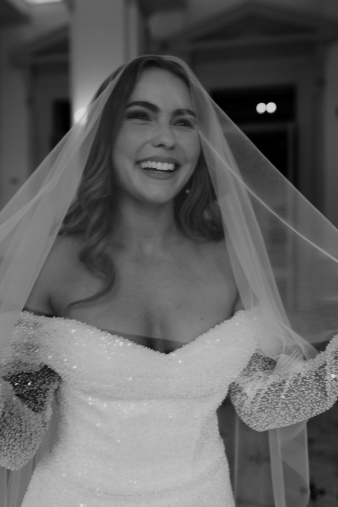 Black & white photo of bride laughing under veil