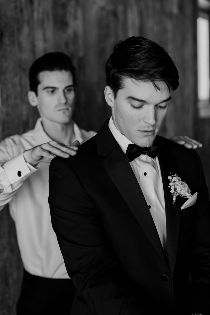 Groom getting into Jacket with best man patting shoulders