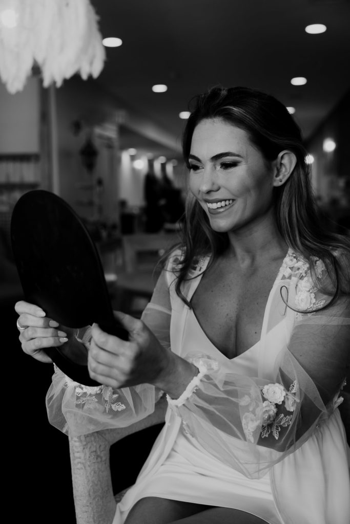 Bride getting ready. Smiles and looks at a mirror to check on her makeup