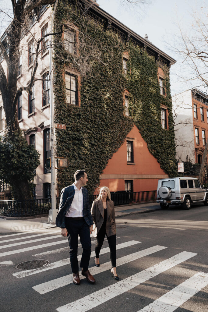 Couple crossing street in Greenwich Village, New York City smiling at each other during New York engagement photo session