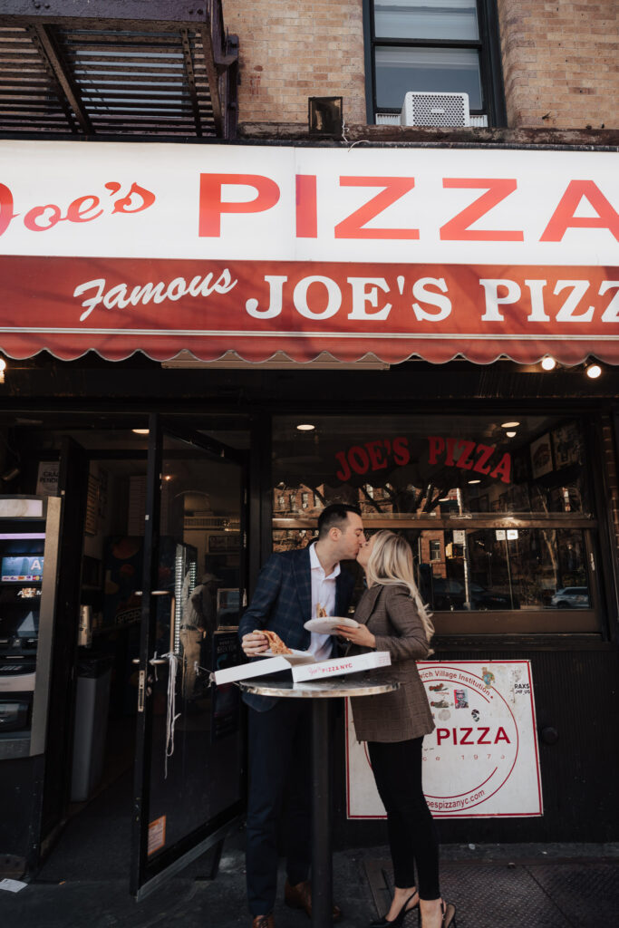 Couple kissing and eating pizza in front of Joe's Pizza in New York City