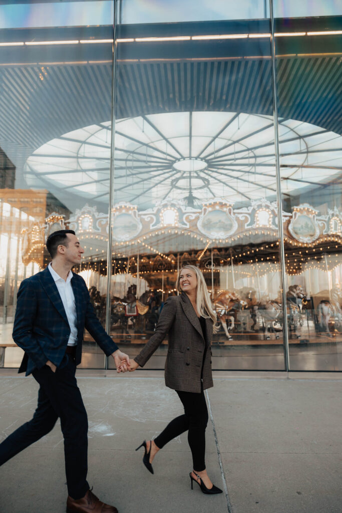 Woman smiling at man walking past Jane's Carousel at their New York engagement photo session