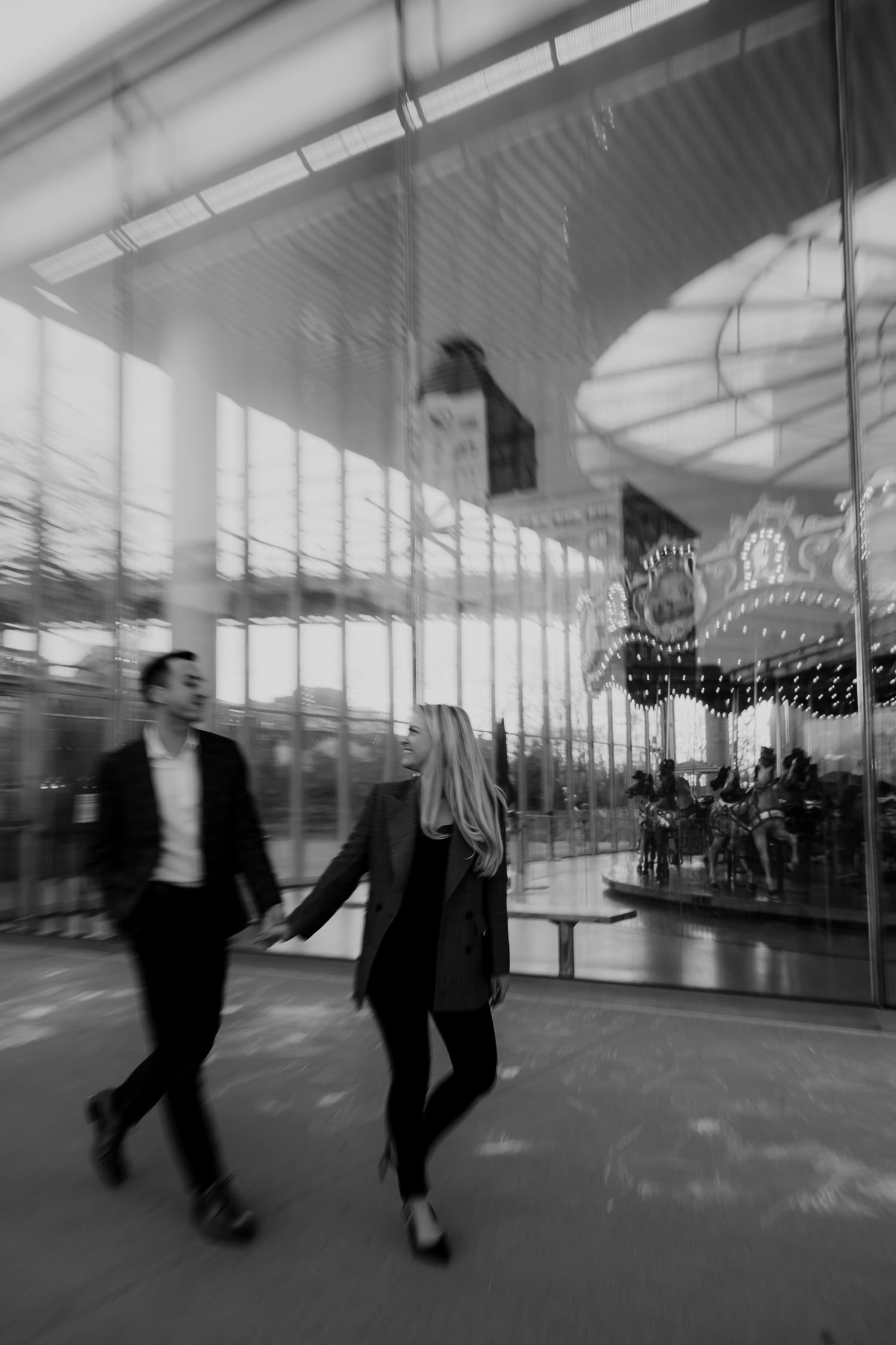 black and white photo of couple walking in front of Jane's Carousel in New York City during engagement photo session