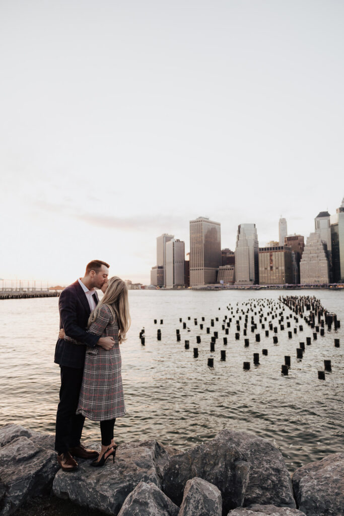 Couple kissing while standing on rocks at the The Granite Prospect with New York Skyline in background. New York Engagement Photo session