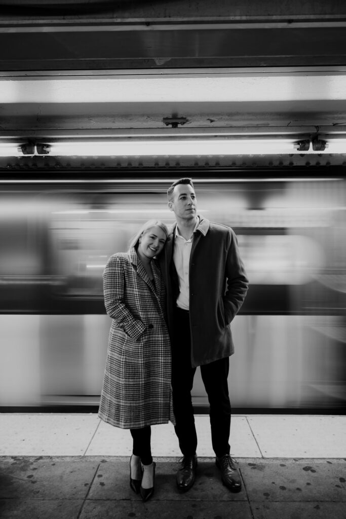 couple standing in front of incoming subway train during New York engagement photo session