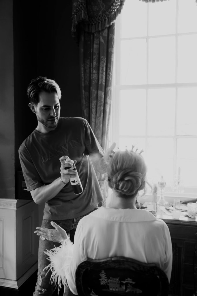 Hair stylist making final touch on bridal hair with hair spray making sure to keep the wedding photography timeline