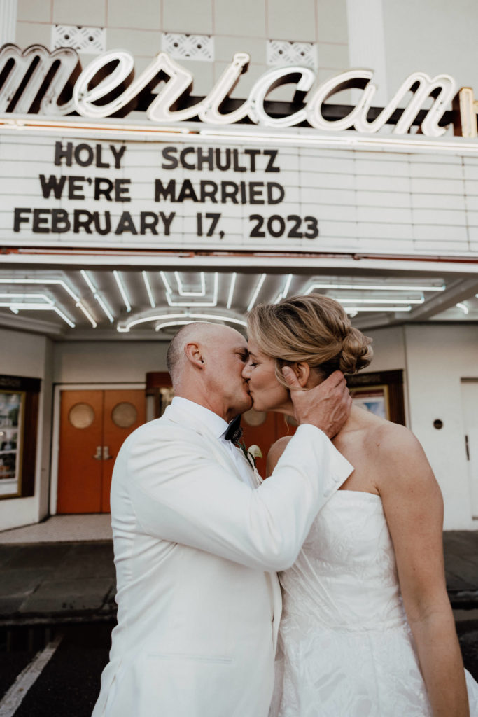 Bride and groom kissing in front of he American Theater in Charleston with their names and dates showing in background