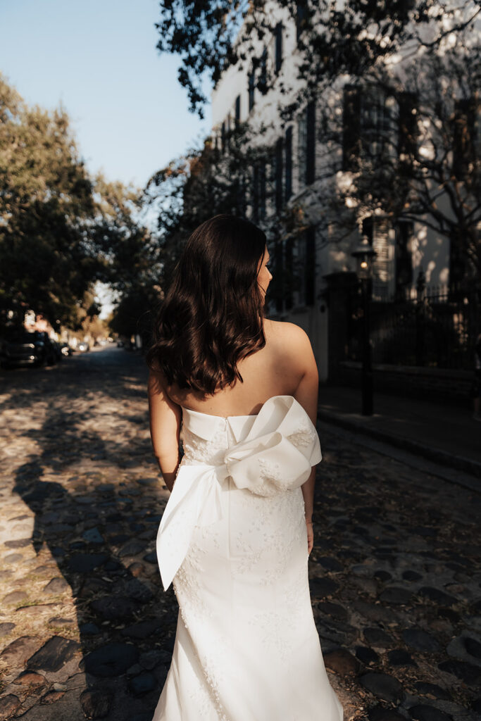 Bride walking down cobblestone street for bridal potraits. Strapless bridal dress with bow on back.