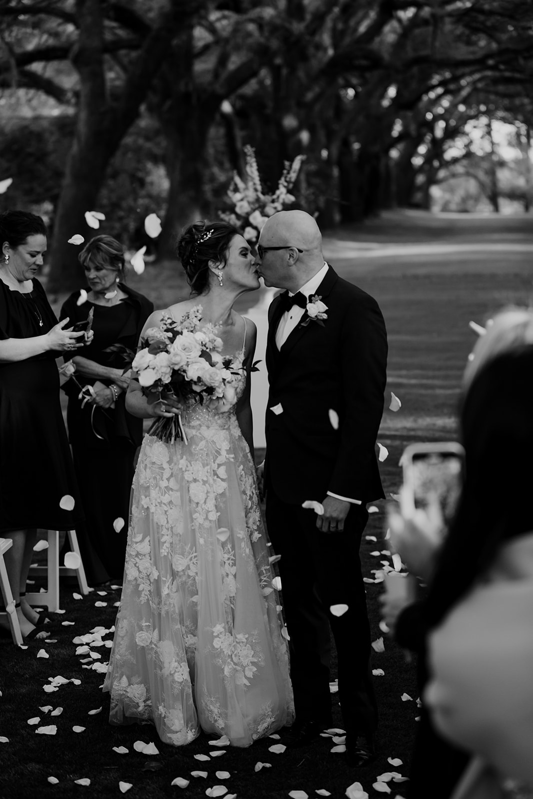 Black and white photo of bride and groom kissing. Rose paddles flying in middle of the aisle at legare waring house wedding
