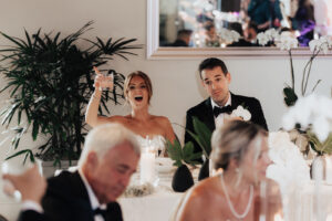 Bride sitting next to groom is toasting to wedding guest from sweetheart table at Cannon Green wedding