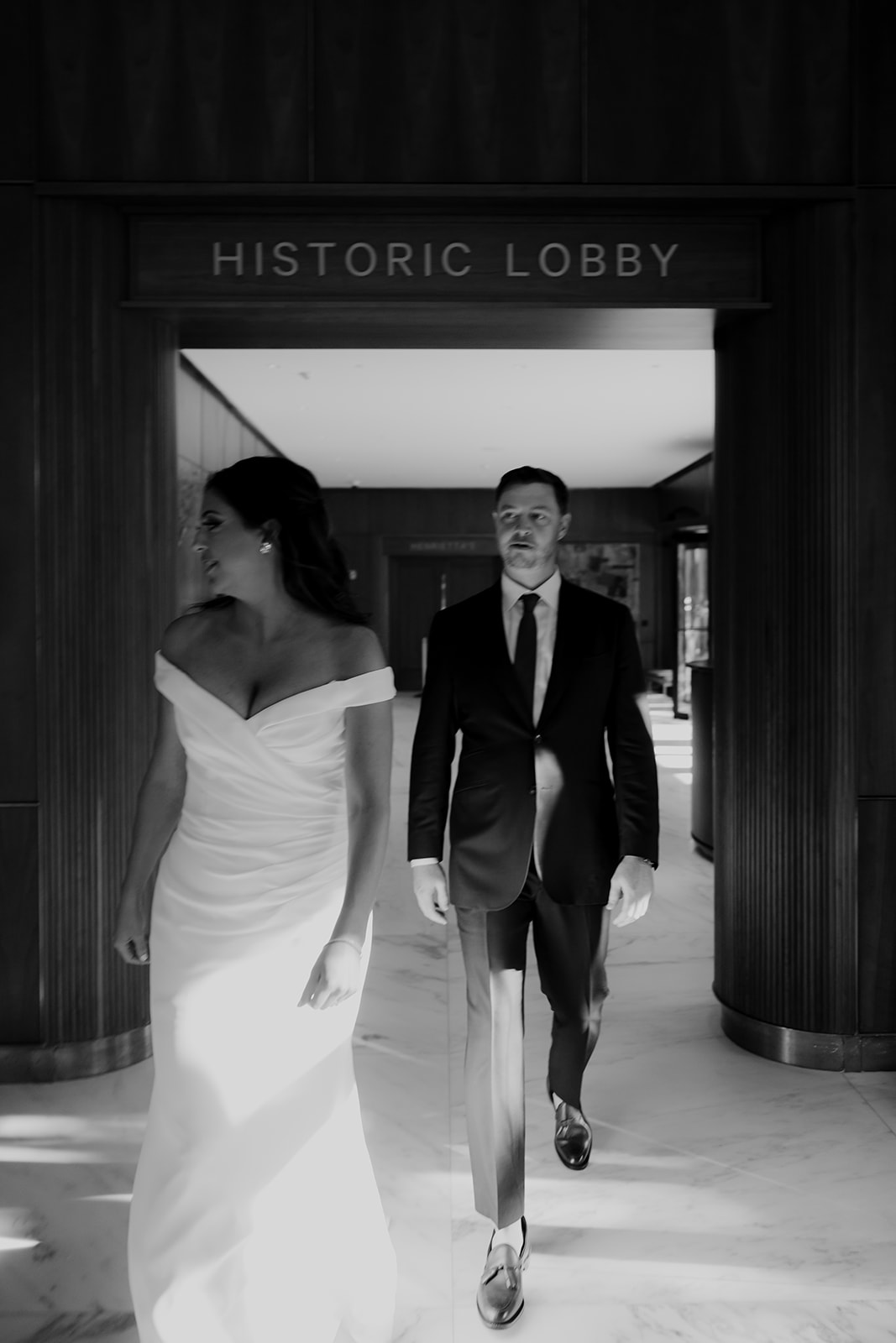 Black and white photo of bride and groom walking in Dewberry hotel lobby