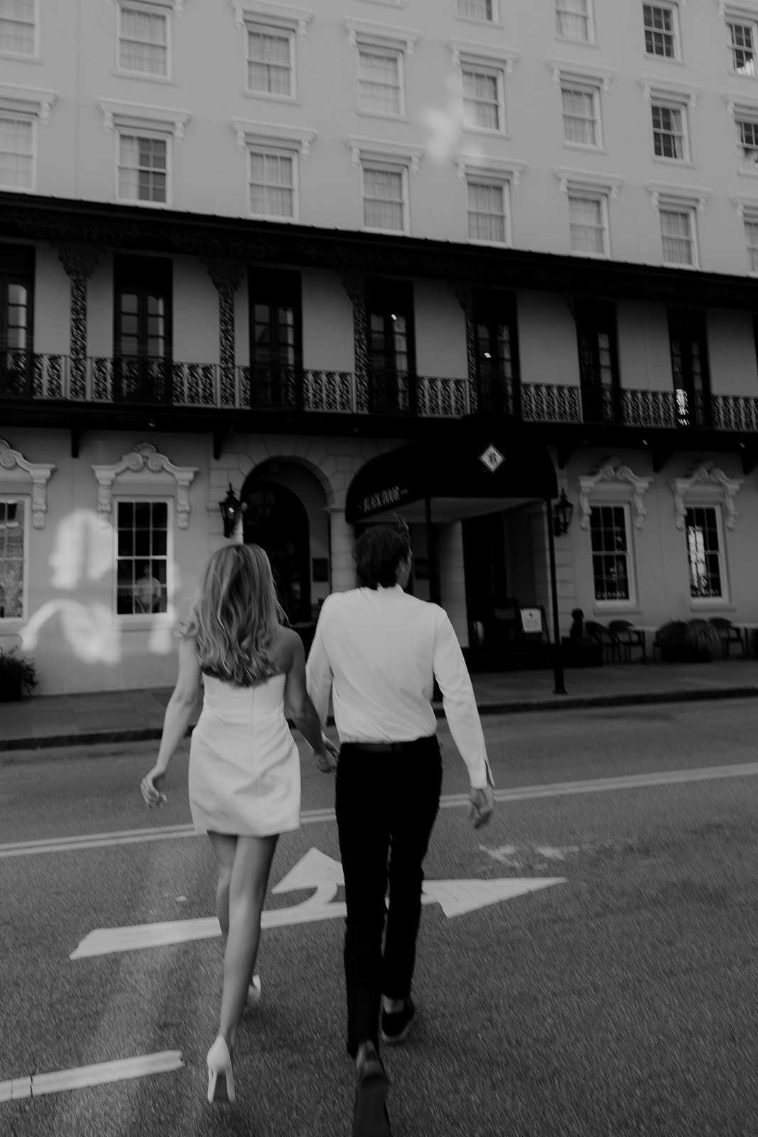 Woman and man walking across street for Charleston Engagement Photos. Millshouse in background