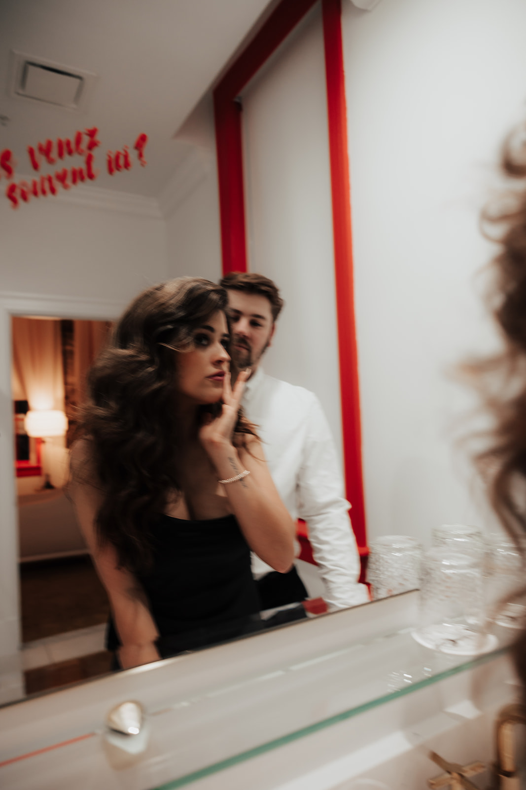 Couple photographed in mirror at vendue Hotel Engagement Session. word written in red on mirror. Man standing behind woman