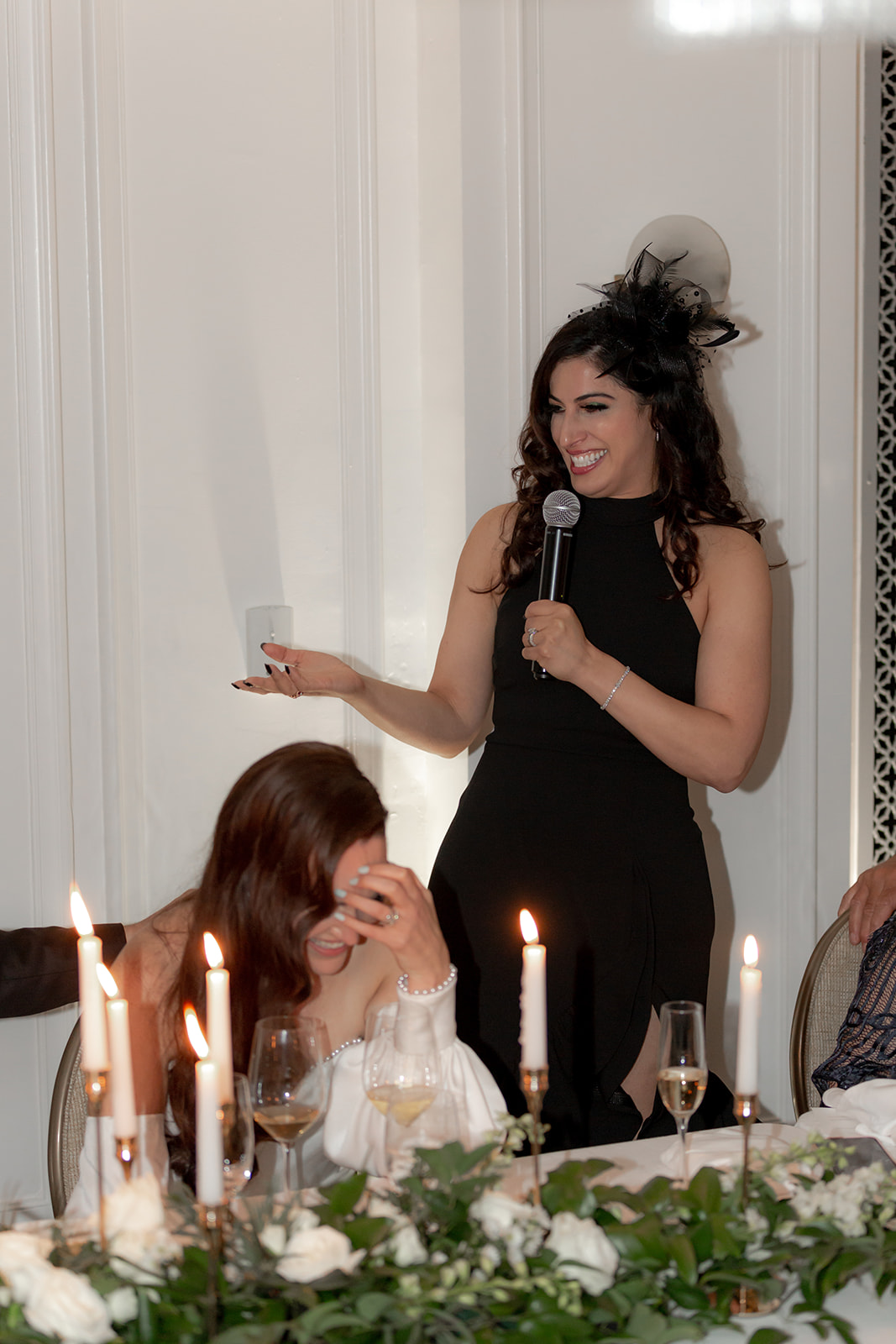 Wedding guest holding speech standing behind bride. bride is laughing.