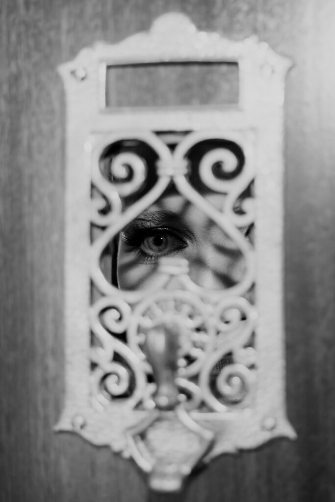 Artsy photo of bride looking through iron ornament on wooden door. Only eye visible and some shadows on face.