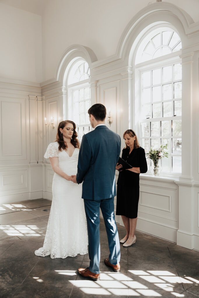 Bride and groom standing during ceremony. Modern white chapel with high windows.