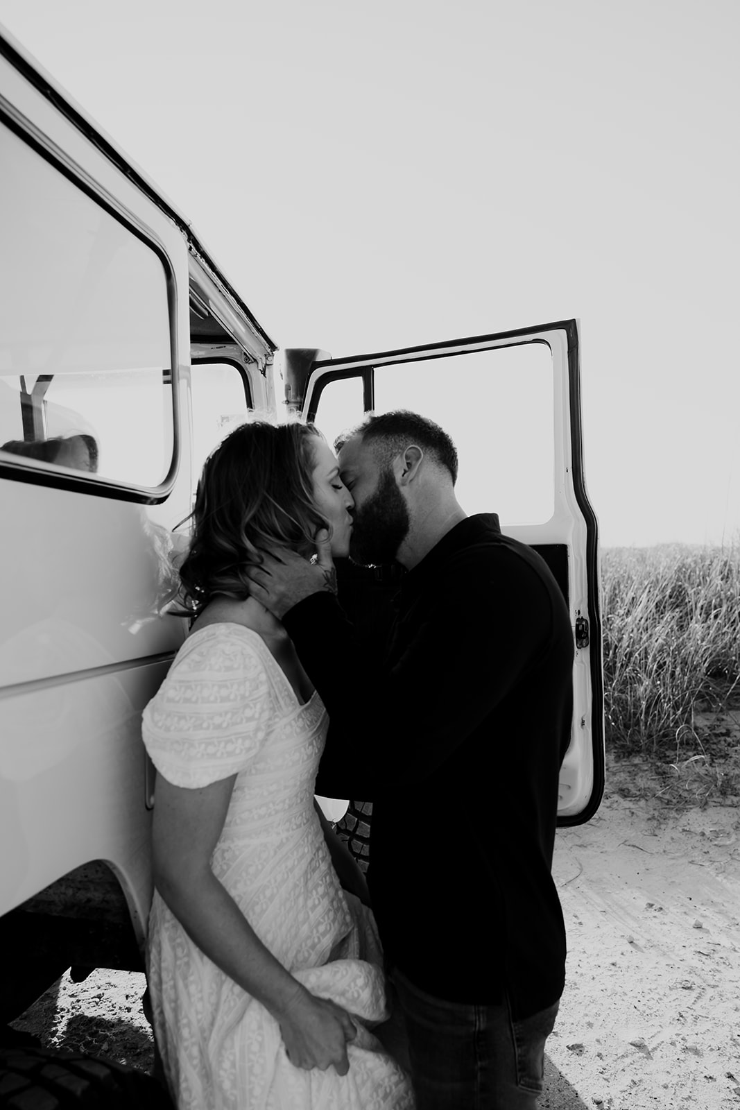 Man kisses woman leaning against car. Sand and dunes in the background