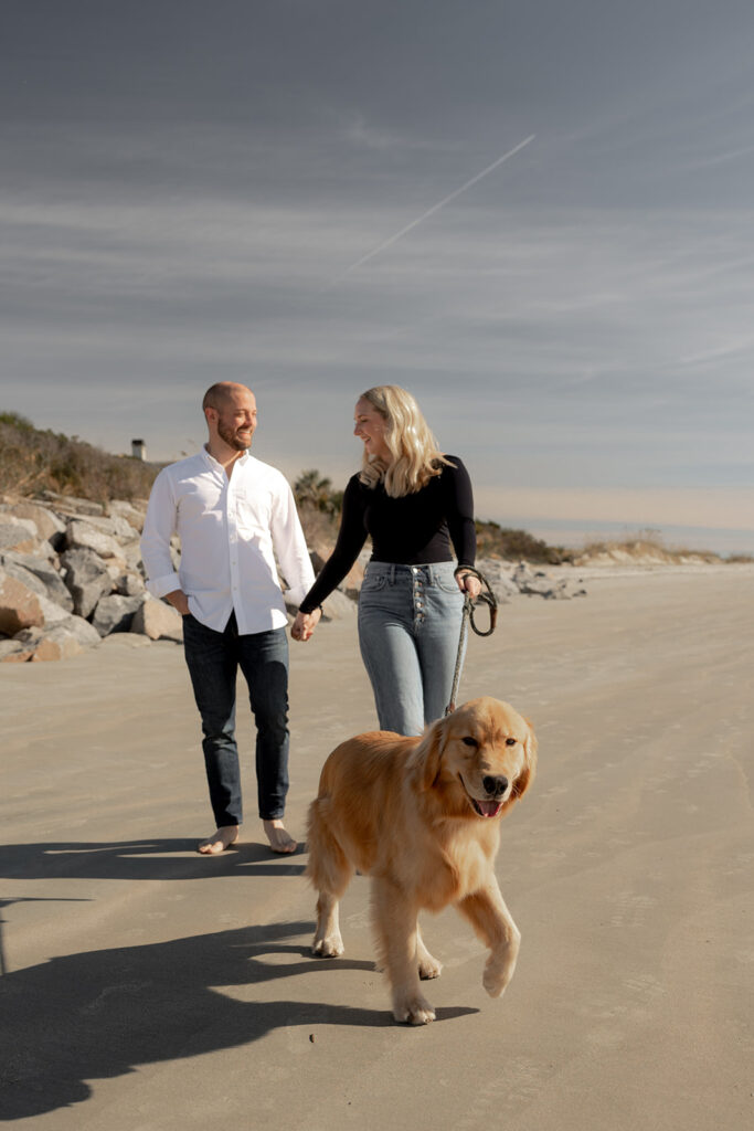 Couple holding hand and walking golden retriever at Seabrook Island Beach for Engagement photos