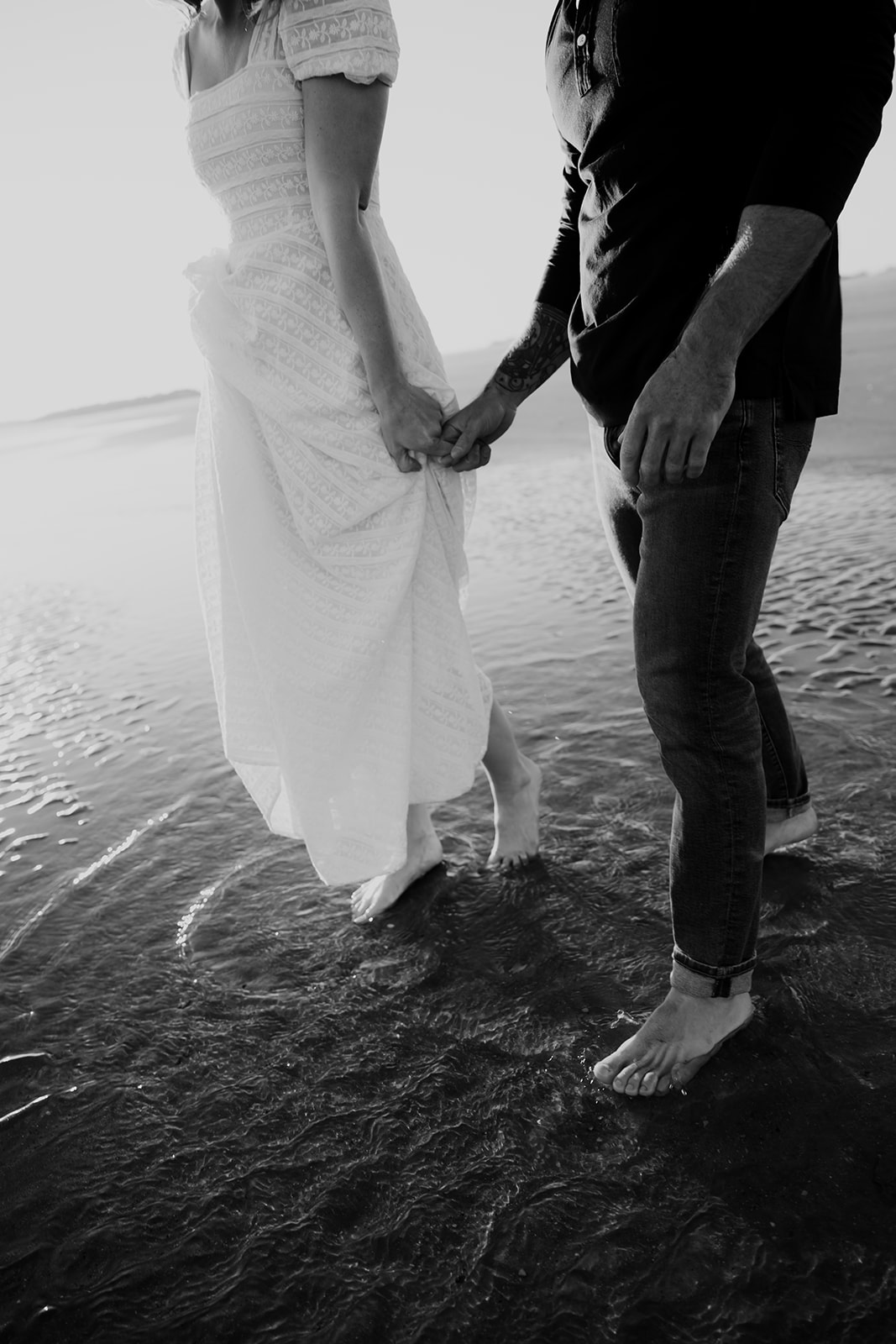Black and white photograph of couple standing in low water holding hands