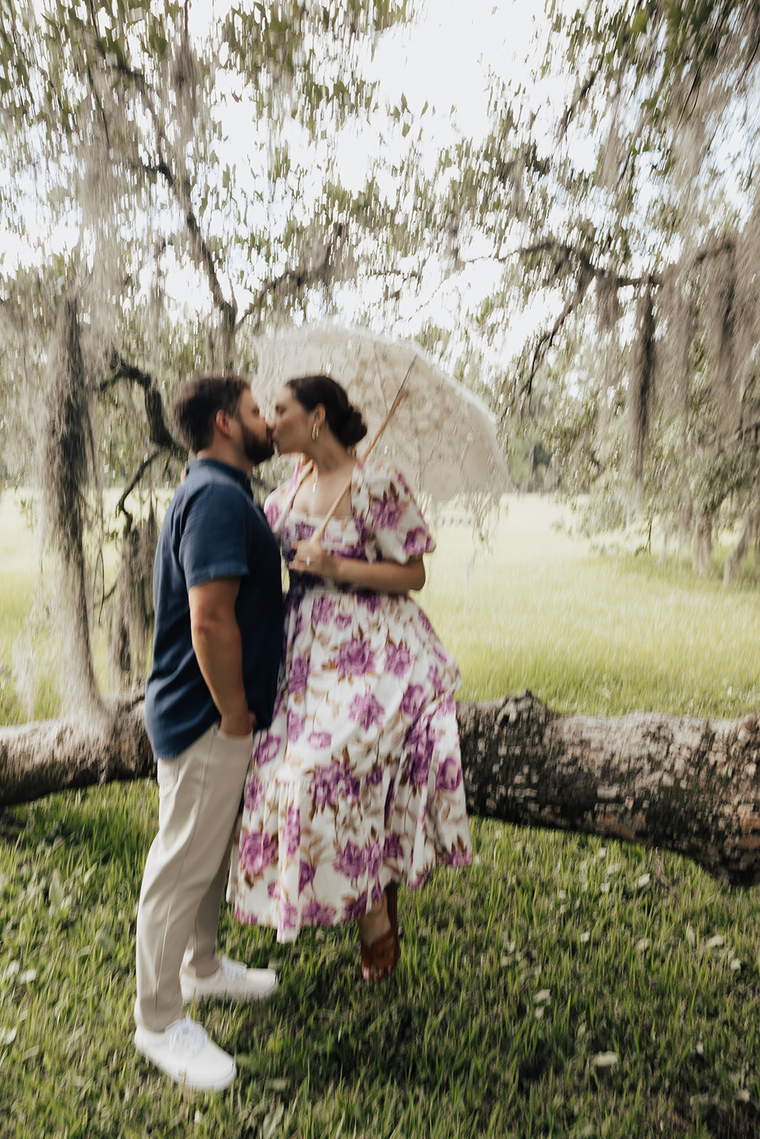 Romantic kiss. Woman sitting on oak tree branch holding parasol. Man stands in front of her and shares a kiss during magnolia plantation proposal