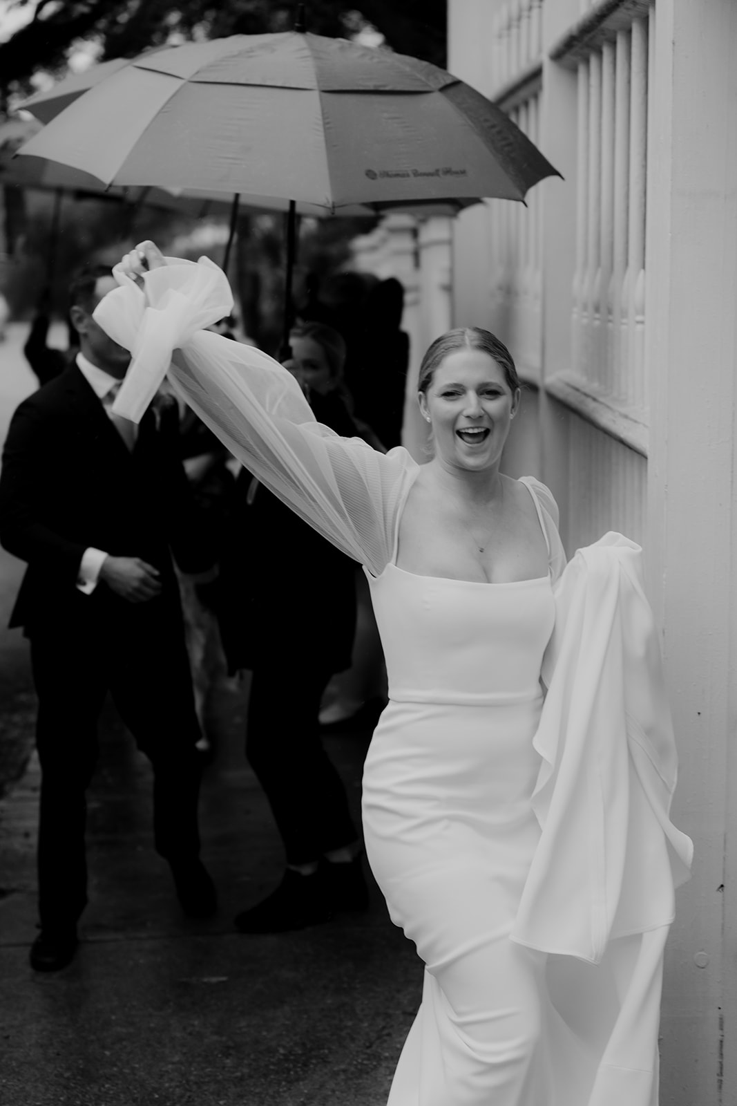 Bride arriving for Wedding at Gov. Thomas Bennett House. Lifting right arm and cheers towards camera. Umbrella and bridal party in the background