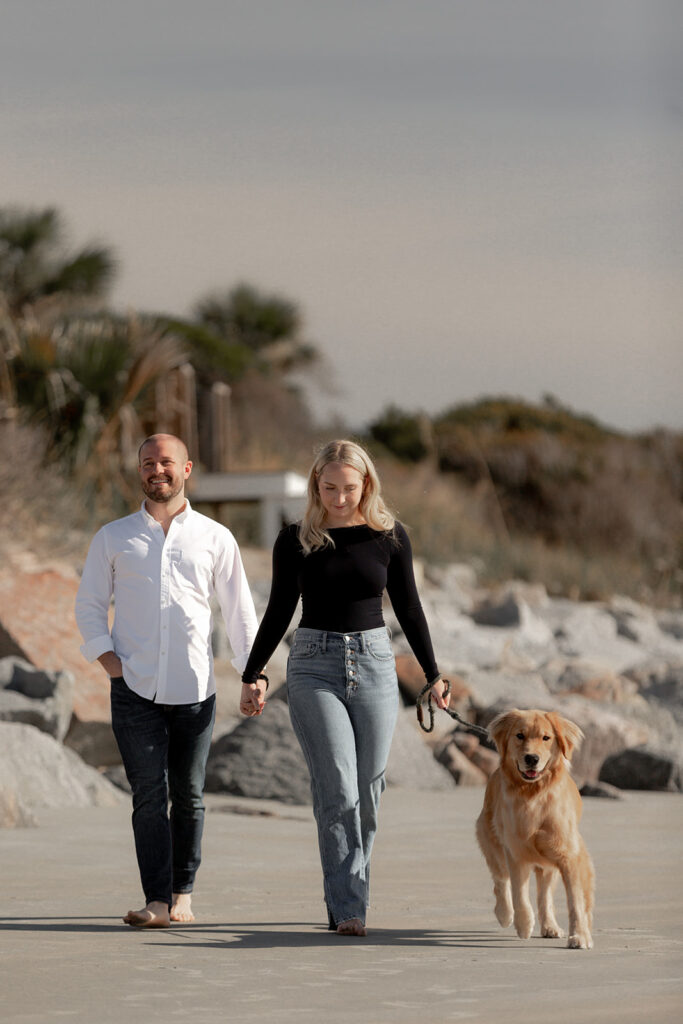 Seabrook Island Beach Engagement with dog. Couple and dog walking towards camera with dunes in background