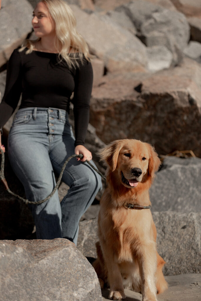 Cute golden retriever looking curiously to the side during Seabrook Island Beach Engagement session. Woman holding leash and stones in the background