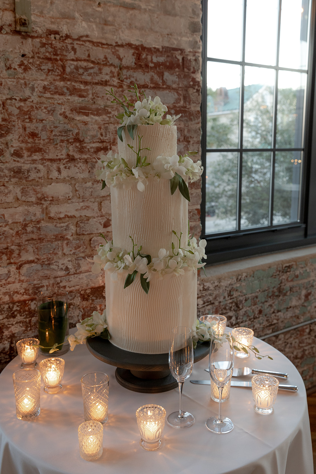 wedding cake in front of a brick wall and surrounded by candles.