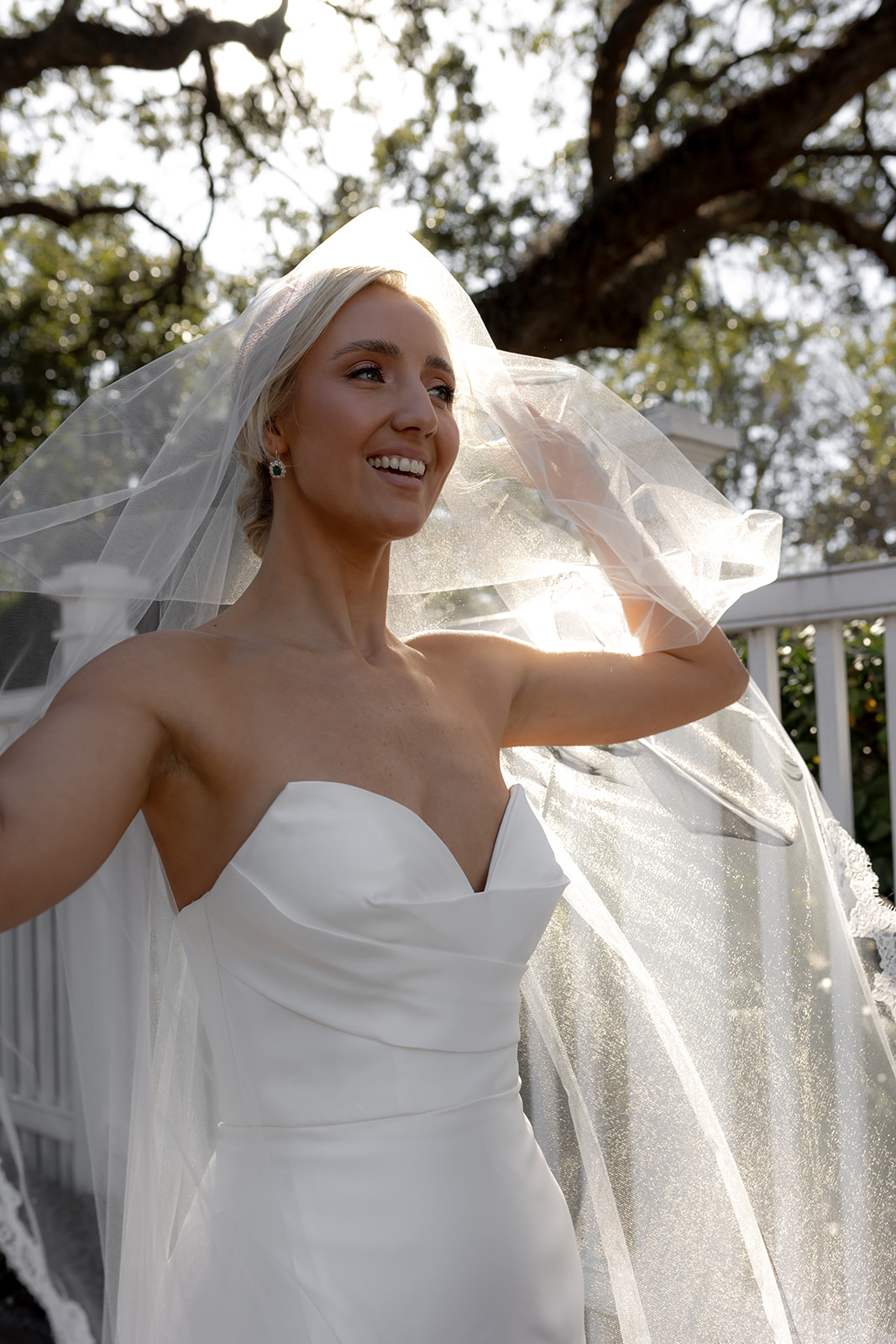 Bride smiling and enjoying wedding dress photo session. Oak tree in background and sunbeams shining through leaves.
