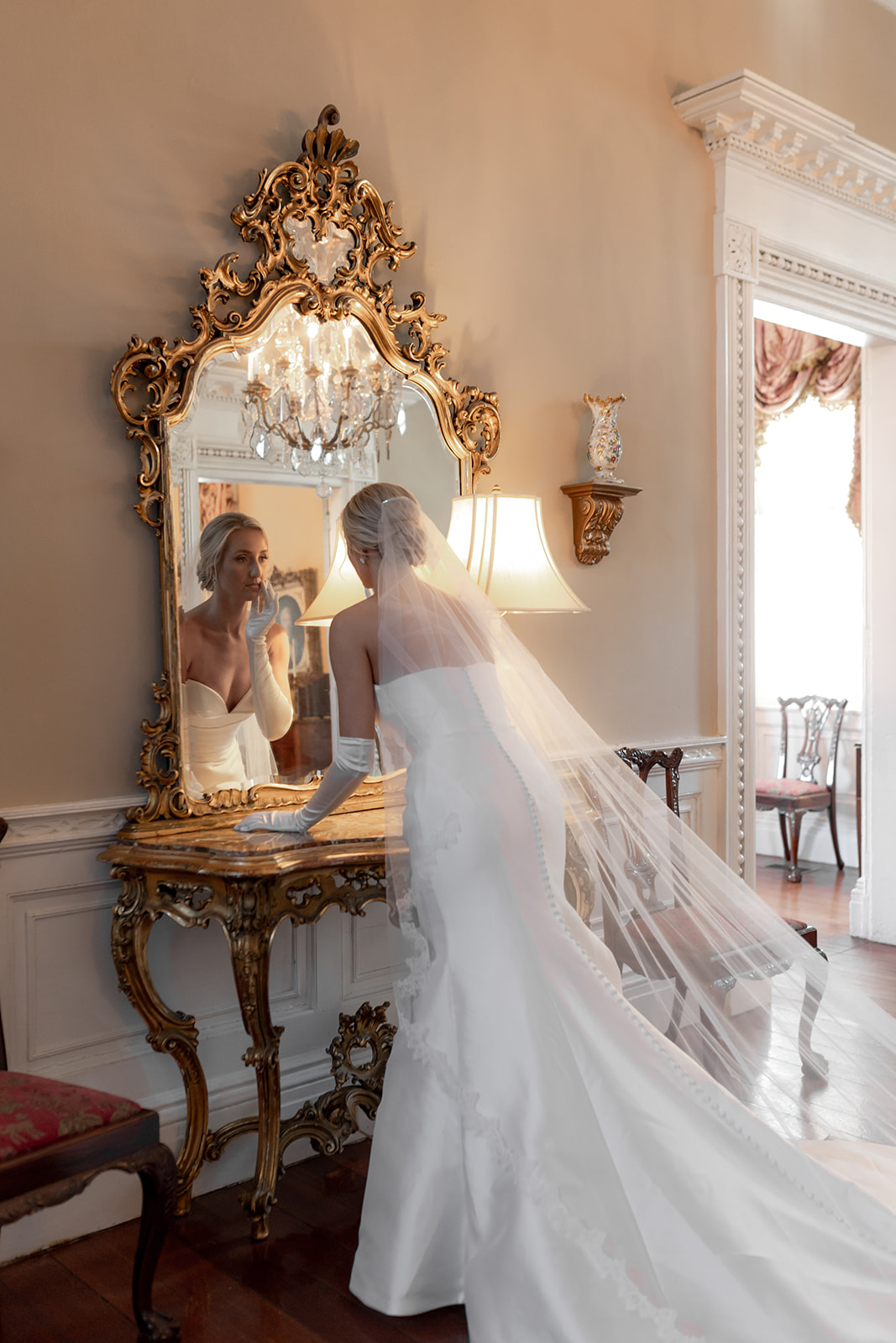 Bride looking into antique mirror with golden frame.