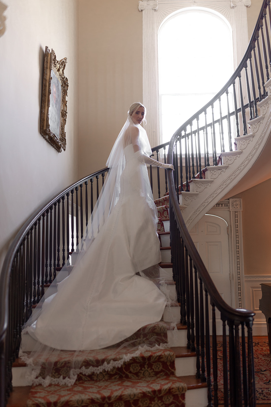 Bride walking up staircase in historic home in Charleston in wedding dress. Looking back.