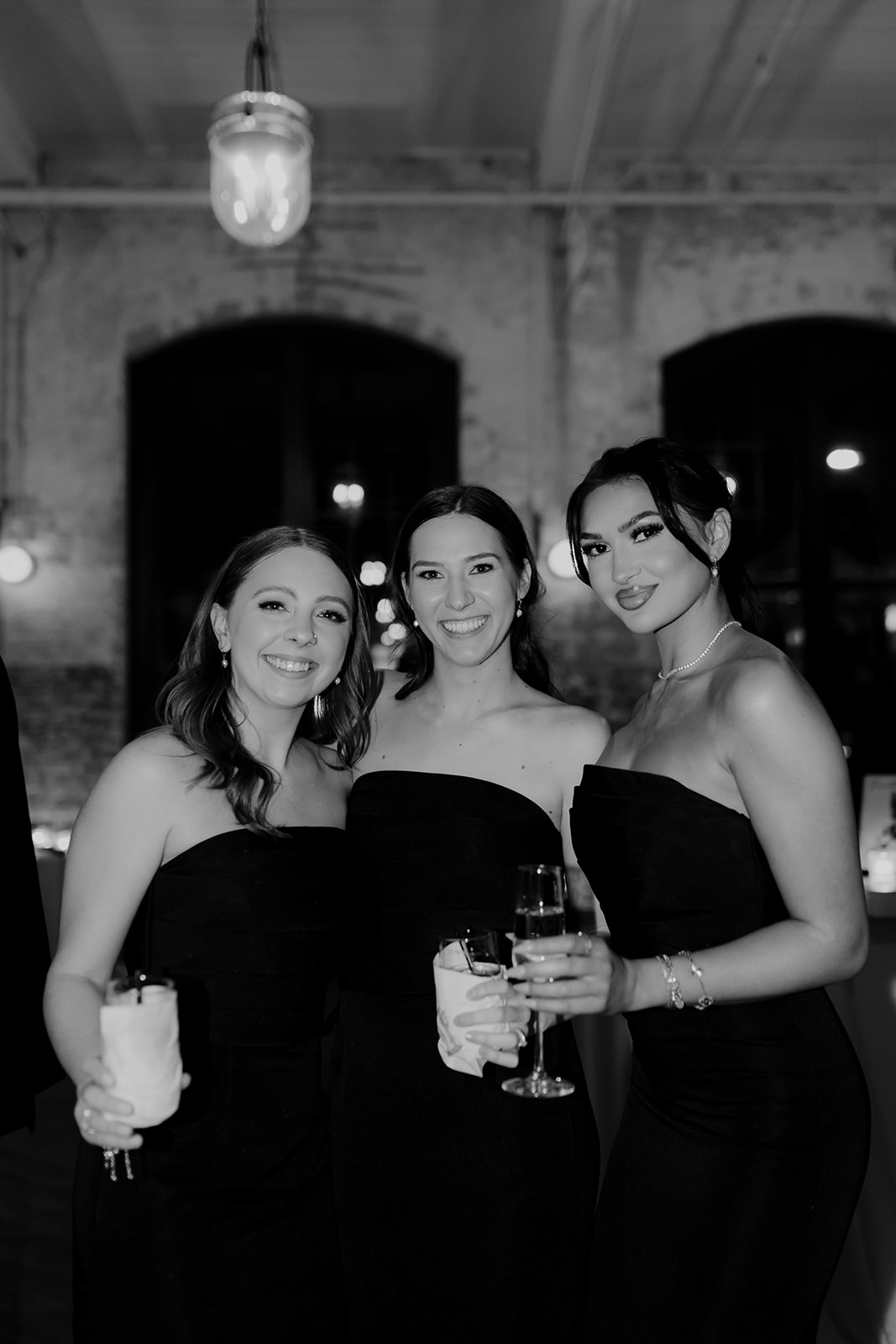 Bridesmaids in black dresses looking at camera and holding drinks at a wedding at Cedar Room Charleston