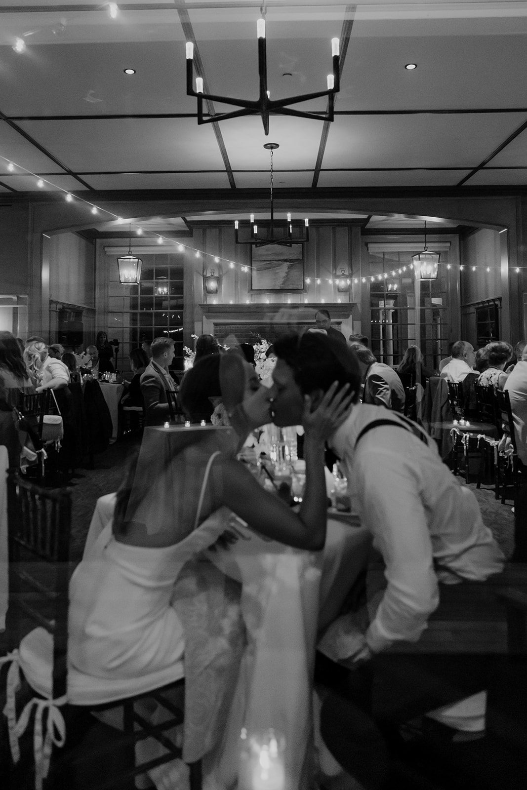 Bride and groom kissing during reception photographed through window