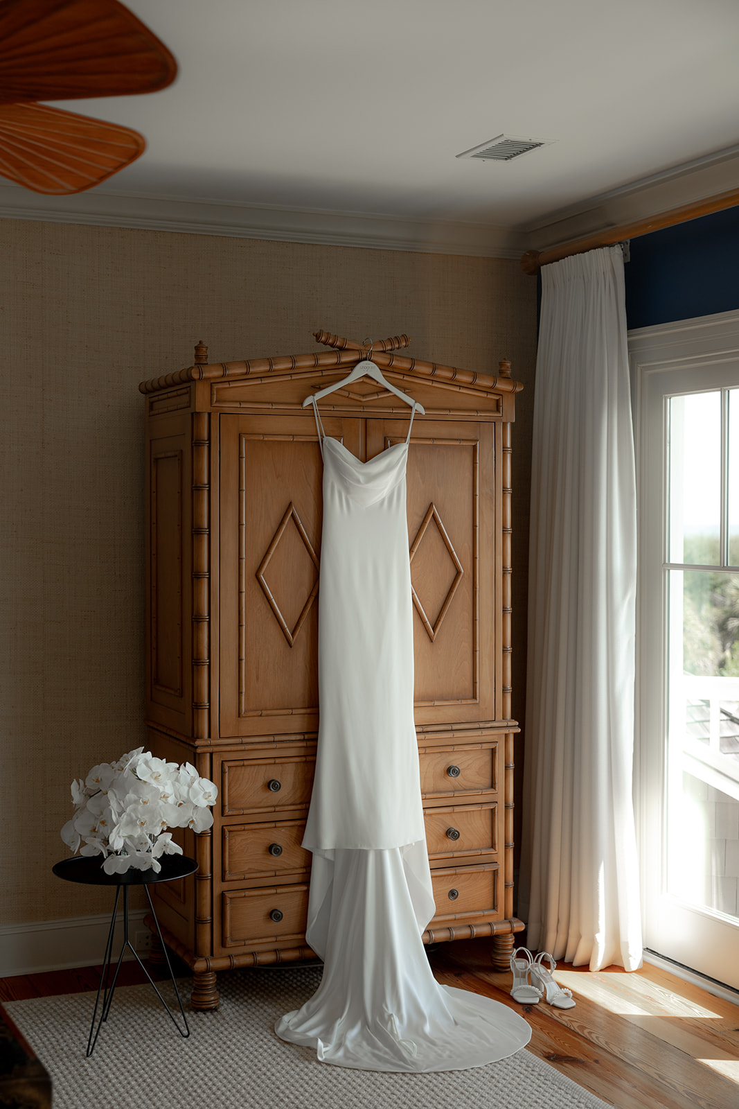 Getting ready for Kiawah Ocean Course wedding. Wedding dress hung at wooden closet with bridal bouquet next to it.