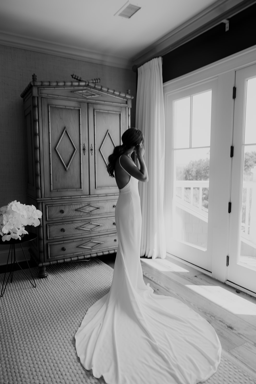 Bride getting ready and putting on her earings while looking towards window.
