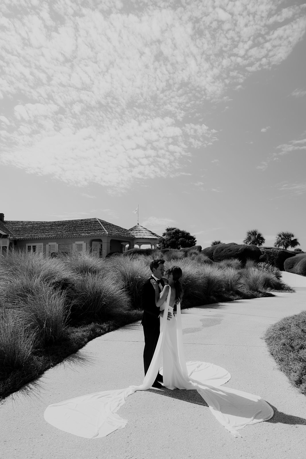 Black and white portrait of bride and groom with muhly grass and Kiawah clubhouse in the background