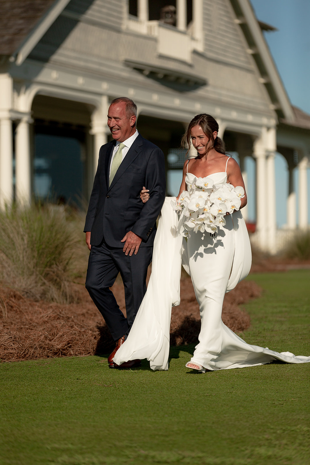 Bride and father of the bride walking towards Kiawah Ocean Course wedding ceremony. Clubhouse in the background.